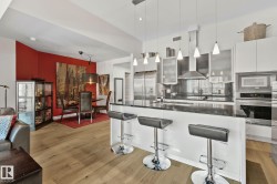 Open-concept kitchen featuring an eat-at island with pendant lighting, stainless steel appliances, and sleek flat-panel cabinetry - 