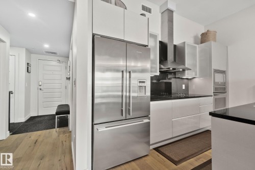 Modern kitchen featuring stainless steel appliances, white cabinetry, black countertops, and a built-in oven and microwave - 201 10388 105 Street, Edmonton, AB 