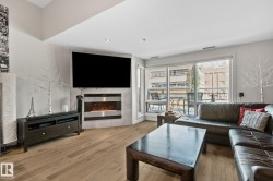 Living area featuring wood-finish flooring, an angular fireplace with stone surround, recessed lighting, and a large sliding glass door opening to an exterior balcony - 