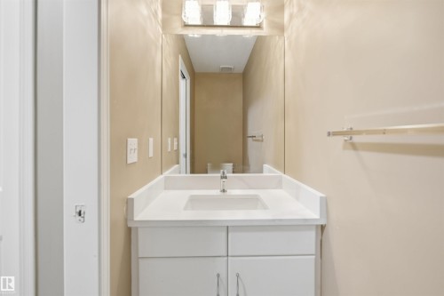 Bathroom featuring a white vanity with two cabinet doors and two drawers, a white countertop with an integrated sink, a chrome faucet, and a large mirror with a three-light vanity fixture - 2610 33A Street, Edmonton, AB - Indoor Photo Showing Bathroom