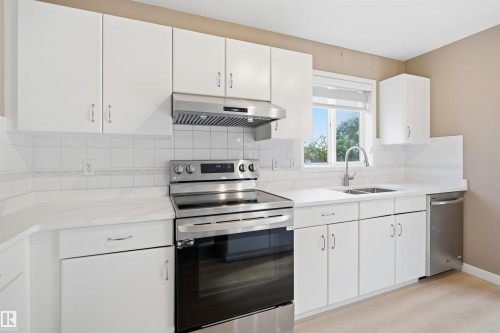 Contemporary kitchen featuring white cabinetry, stainless steel appliances, a tile backsplash, and light-toned countertops - 2610 33A Street, Edmonton, AB - Indoor Photo Showing Kitchen With Double Sink