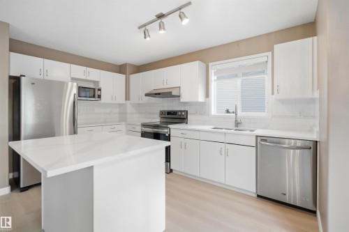 Kitchen featuring a central island with a white countertop, white cabinetry, stainless steel appliances, a subway tile backsplash, and light wood-finish flooring - 2610 33A Street, Edmonton, AB - Indoor Photo Showing Kitchen With Upgraded Kitchen