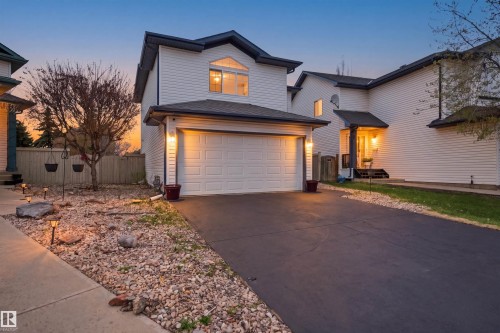 White siding exterior with an attached garage, paved driveway, and stone landscaping - 2610 33A Street, Edmonton, AB - Outdoor With Facade