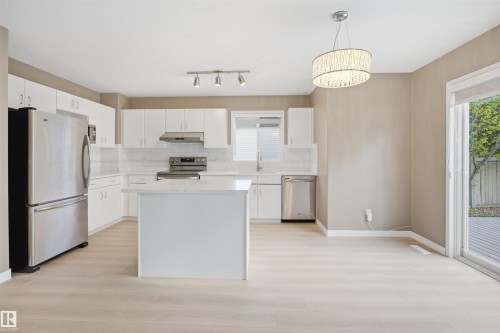 Kitchen featuring white cabinetry, light-toned wood-finish flooring, stainless steel appliances, a center island with a light countertop, and a sliding glass door providing exterior access - 2610 33A Street, Edmonton, AB - Indoor Photo Showing Kitchen With Upgraded Kitchen