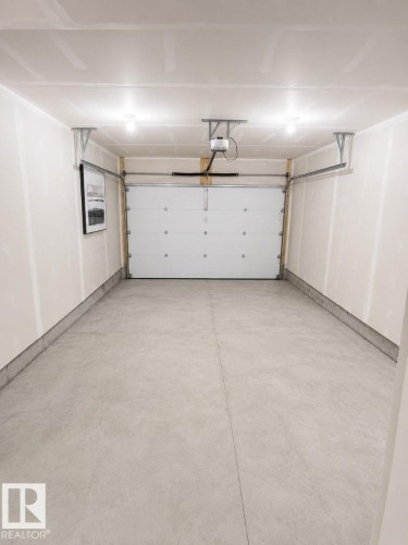Concrete flooring and white painted walls characterize this garage space, featuring a sectional garage door, overhead lighting, and an automatic garage door opener system - 311 32 Street, Edmonton, AB 