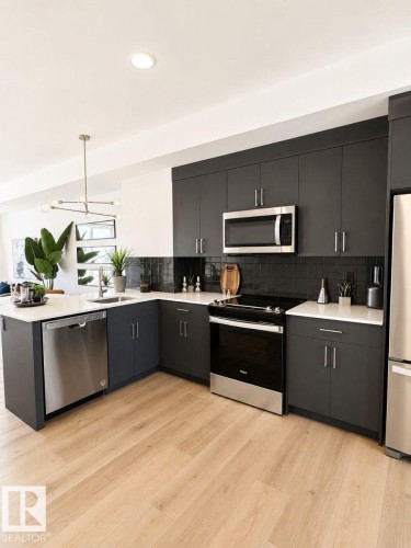 Modern kitchen featuring dark cabinetry, stainless steel appliances, light wood-finish flooring, white countertops, and a subway tile backsplash - 311 32 Street, Edmonton, AB 