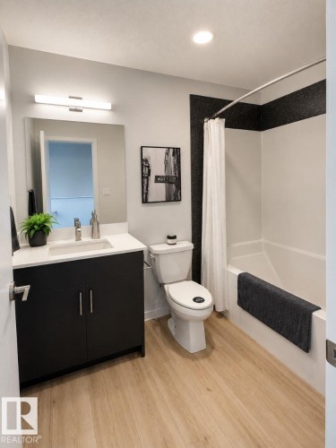 Contemporary bathroom featuring a dark vanity with a white countertop and rectangular undermount sink, wood-finish flooring, recessed lighting, and a white tub with dark accent wall - 311 32 Street, Edmonton, AB 
