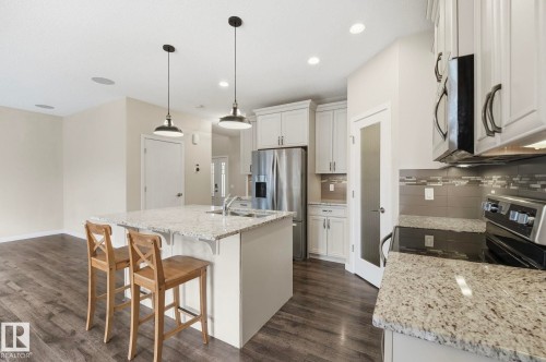 Open-concept kitchen featuring white cabinetry, granite countertops, stainless steel appliances, wood-finish flooring, and pendant lighting over the island - 33 Riviere Terrace, St. Albert, AB 