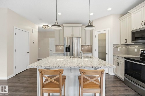 Kitchen featuring a large island with a light-toned countertop, stainless steel appliances, white cabinetry with dark hardware, a patterned backsplash, and wood-finish flooring - 33 Riviere Terrace, St. Albert, AB 