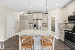 Kitchen featuring a large island with a light-toned countertop, stainless steel appliances, white cabinetry with dark hardware, a patterned backsplash, and wood-finish flooring - 