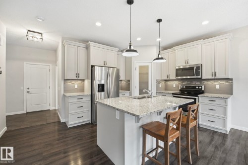 Modern kitchen featuring a central island with integrated sink, stainless steel appliances, light cabinetry, wood-finish flooring, and pendant lighting - 33 Riviere Terrace, St. Albert, AB 