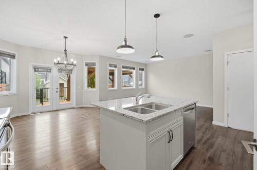 Bright open-concept kitchen and dining area featuring a central island with a double sink, stainless steel dishwasher, and light-toned granite countertop - 33 Riviere Terrace, St. Albert, AB 