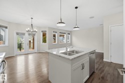 Bright open-concept kitchen and dining area featuring a central island with a double sink, stainless steel dishwasher, and light-toned granite countertop - 