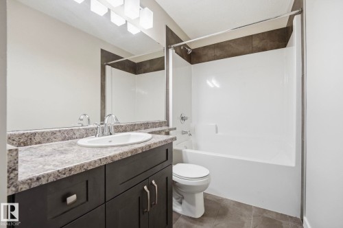 Bathroom featuring a white bathtub and shower surround, a dark wood-finish vanity with a light speckled countertop, and a large mirror with overhead vanity lighting - 33 Riviere Terrace, St. Albert, AB 
