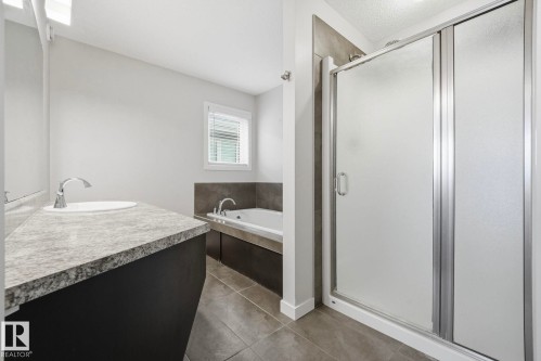 Bathroom featuring a large vanity with an integrated sink, a built-in bathtub with a tiled surround, a separate shower enclosure with frosted glass, and tiled flooring - 33 Riviere Terrace, St. Albert, AB 