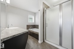 Bathroom featuring a large vanity with an integrated sink, a built-in bathtub with a tiled surround, a separate shower enclosure with frosted glass, and tiled flooring - 