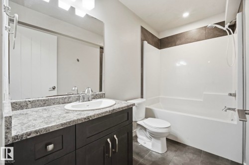 Modern bathroom featuring a dark wood-finish vanity with a light speckled countertop, an integrated oval sink, and a large wall-mounted mirror - 33 Riviere Terrace, St. Albert, AB 