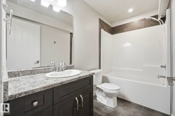 Modern bathroom featuring a dark wood-finish vanity with a light speckled countertop, an integrated oval sink, and a large wall-mounted mirror - 