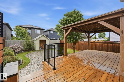 Expansive outdoor living area featuring a covered wooden deck, a paved patio, a storage shed, and mature landscaping - 33 Riviere Terrace, St. Albert, AB 