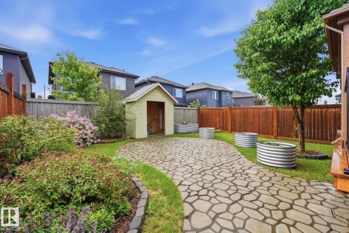 Landscaped backyard featuring a stone-look paver patio, a freestanding shed, raised garden beds, and mature trees - 33 Riviere Terrace, St. Albert, AB 