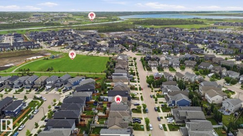 Aerial perspective of a residential community with diverse single-family homes, organized street layouts, a large green space, and a distant body of water - 33 Riviere Terrace, St. Albert, AB 