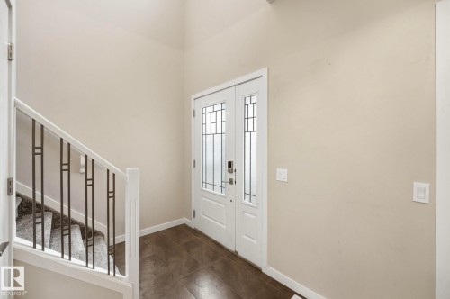 Entryway featuring a double door with decorative glass inserts, ceramic tile flooring, and a staircase with a white wood railing and metal balusters - 33 Riviere Terrace, St. Albert, AB 