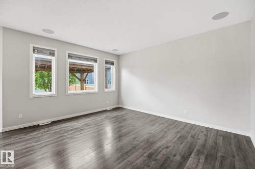 Spacious room featuring wood-finish flooring, three large windows, white trim, and ceiling-mounted speakers - 33 Riviere Terrace, St. Albert, AB 