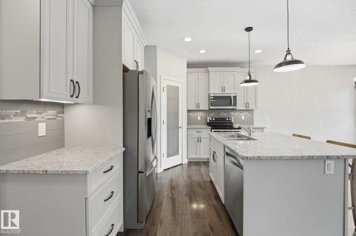 Contemporary kitchen featuring light gray cabinetry, stainless steel appliances, speckled countertops, and wood-finish flooring - 33 Riviere Terrace, St. Albert, AB 