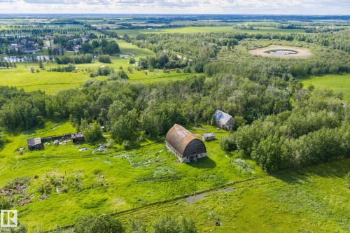 Expansive rural landscape featuring a large arched-roof barn and additional structures amidst green fields and mature trees - 23327 Twp Rd 510, Rural Leduc County, AB 