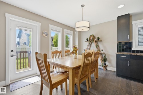 Open-concept dining area featuring dark wood-finish flooring, a contemporary drum pendant light, and abundant natural light from multiple windows and a glass-paneled door - 5430 Edworthy Way, Edmonton, AB - Indoor Photo Showing Dining Room