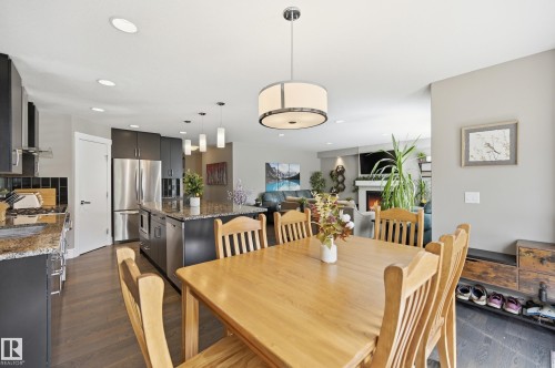 Open-concept living space featuring wood-finish flooring, a kitchen with dark cabinetry and a stone-finish island, recessed lighting, and a living area with a fireplace - 5430 Edworthy Way, Edmonton, AB - Indoor Photo Showing Dining Room