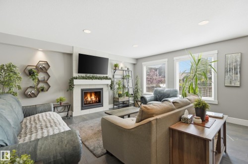 Living area featuring a fireplace with a tile surround, dark wood-finish flooring, recessed lighting, and multiple windows with white blinds - 5430 Edworthy Way, Edmonton, AB - Indoor Photo Showing Living Room With Fireplace