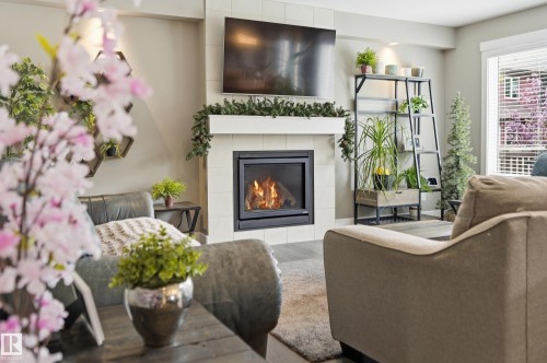 Living area featuring a tiled fireplace with a white mantel, overhead television mount, and a large window with blinds - 5430 Edworthy Way, Edmonton, AB - Indoor Photo Showing Living Room With Fireplace