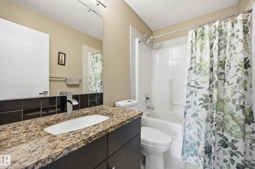 Bathroom featuring a granite countertop vanity with an undermount sink and chrome faucet, a large wall mirror, and a full-size bathtub with a shower - 5430 Edworthy Way, Edmonton, AB - Indoor Photo Showing Bathroom