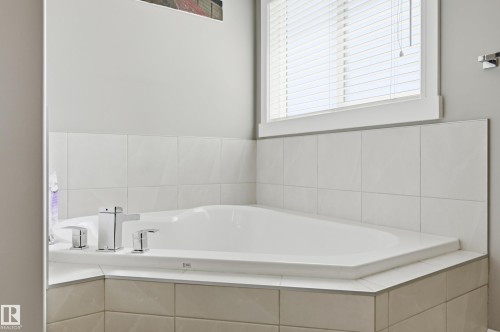 Corner soaking tub with polished chrome fixtures, surrounded by white wall tile and a coordinating tile tub deck - 5430 Edworthy Way, Edmonton, AB - Indoor Photo Showing Bathroom