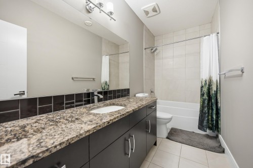 Bathroom featuring a large vanity with a granite-style countertop, undermount sink, and dark wood-finish cabinetry with brushed nickel hardware - 5430 Edworthy Way, Edmonton, AB - Indoor Photo Showing Bathroom