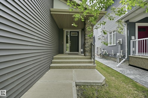 Inviting entryway featuring a dark wood door with glass inserts, concrete steps, a stone pillar, and dark gray horizontal siding - 5430 Edworthy Way, Edmonton, AB - Outdoor