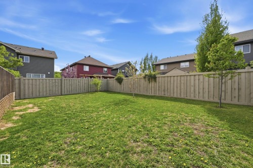 Expansive backyard featuring a full perimeter privacy fence with vertical wood planks, a grass lawn, and young trees - 5430 Edworthy Way, Edmonton, AB - Outdoor