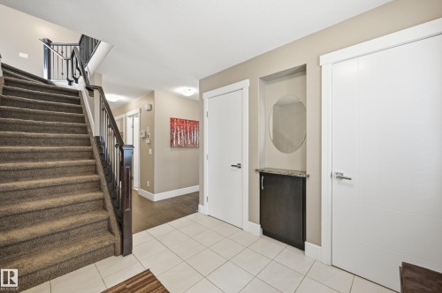 Entryway featuring light-toned tile flooring, a carpeted staircase with dark wood newel posts and metal balusters, and a built-in niche with a dark cabinet and stone countertop - 5430 Edworthy Way, Edmonton, AB - Indoor Photo Showing Other Room