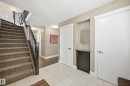 Entryway featuring light-toned tile flooring, a carpeted staircase with dark wood newel posts and metal balusters, and a built-in niche with a dark cabinet and stone countertop - 5430 Edworthy Way, Edmonton, AB  - Indoor Photo Showing Other Room 