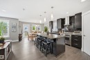 Modern kitchen featuring dark cabinetry, stainless steel appliances, a large center island with seating, pendant lighting, and wood-finish flooring - 5430 Edworthy Way, Edmonton, AB  - Indoor Photo Showing Other Room 