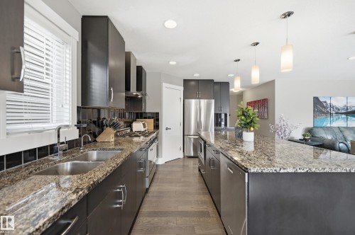 Open-concept kitchen featuring dark cabinetry, stainless steel appliances, granite countertops, and wood-finish flooring - 5430 Edworthy Way, Edmonton, AB - Indoor Photo Showing Kitchen With Stainless Steel Kitchen With Double Sink With Upgraded Kitchen