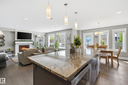 Kitchen island with a polished granite countertop, integrated microwave, and pendant lighting - 5430 Edworthy Way, Edmonton, AB - Indoor With Fireplace
