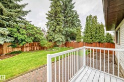 Outdoor deck with white railing, wood-finish flooring, a paved patio, a manicured lawn, and mature perimeter trees - 
