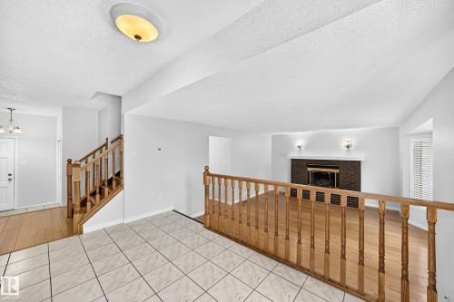 Open-concept interior featuring light wood-finish flooring, a brick-surround fireplace with a white mantel, and a bay window with blinds - 9843 188 Street, Edmonton, AB 