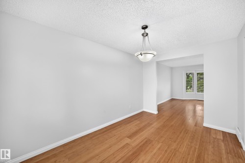 Spacious interior featuring wood-finish flooring, a contemporary pendant light fixture, crisp white walls, and a large window providing a verdant backdrop - 9843 188 Street, Edmonton, AB 