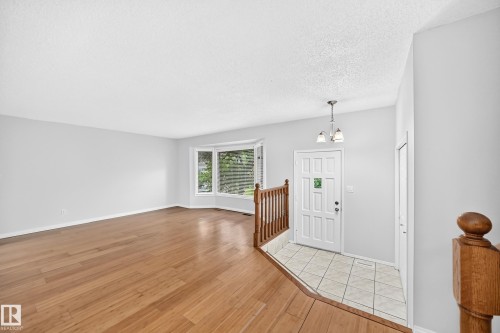 Spacious living area featuring wood-finish flooring, a bay window with multiple panes, and light gray wall paint - 9843 188 Street, Edmonton, AB 