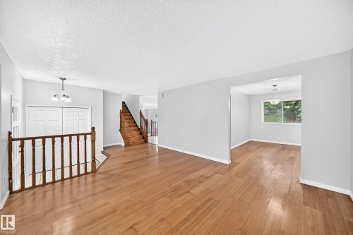 Spacious interior featuring wood-finish flooring, a prominent wooden staircase, a white balustrade, and a recessed room with a large window - 9843 188 Street, Edmonton, AB 
