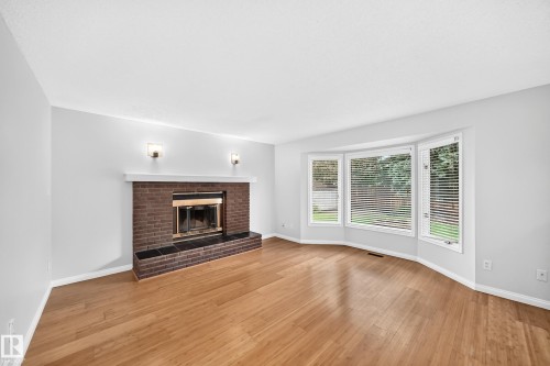Living space featuring wood-finish flooring, a brick fireplace with a white mantel, and a bay window - 9843 188 Street, Edmonton, AB 