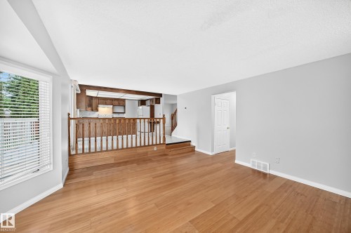 Living area with wood-finish flooring, light grey walls, and a large window with blinds - 9843 188 Street, Edmonton, AB 